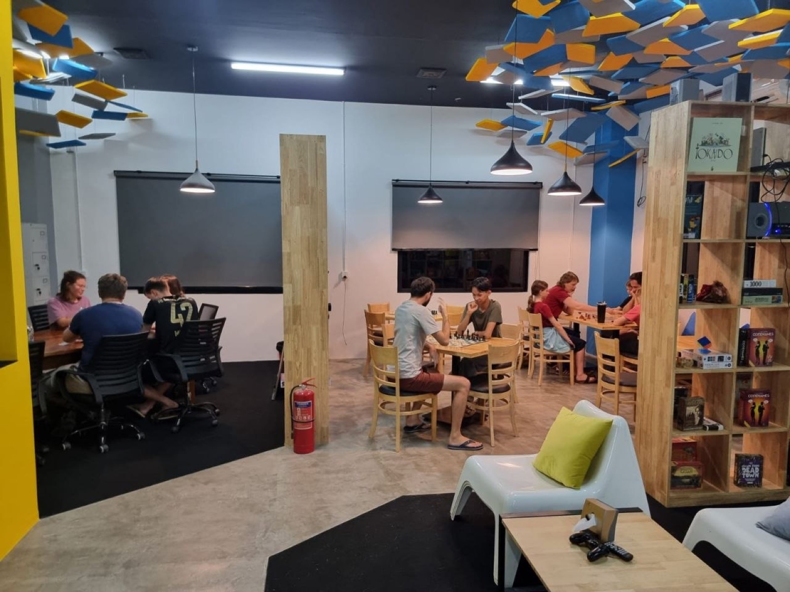 Inside Level Up on a busy game night, players at tables under the hexagon light rig, board-game shelves and lounge seating
