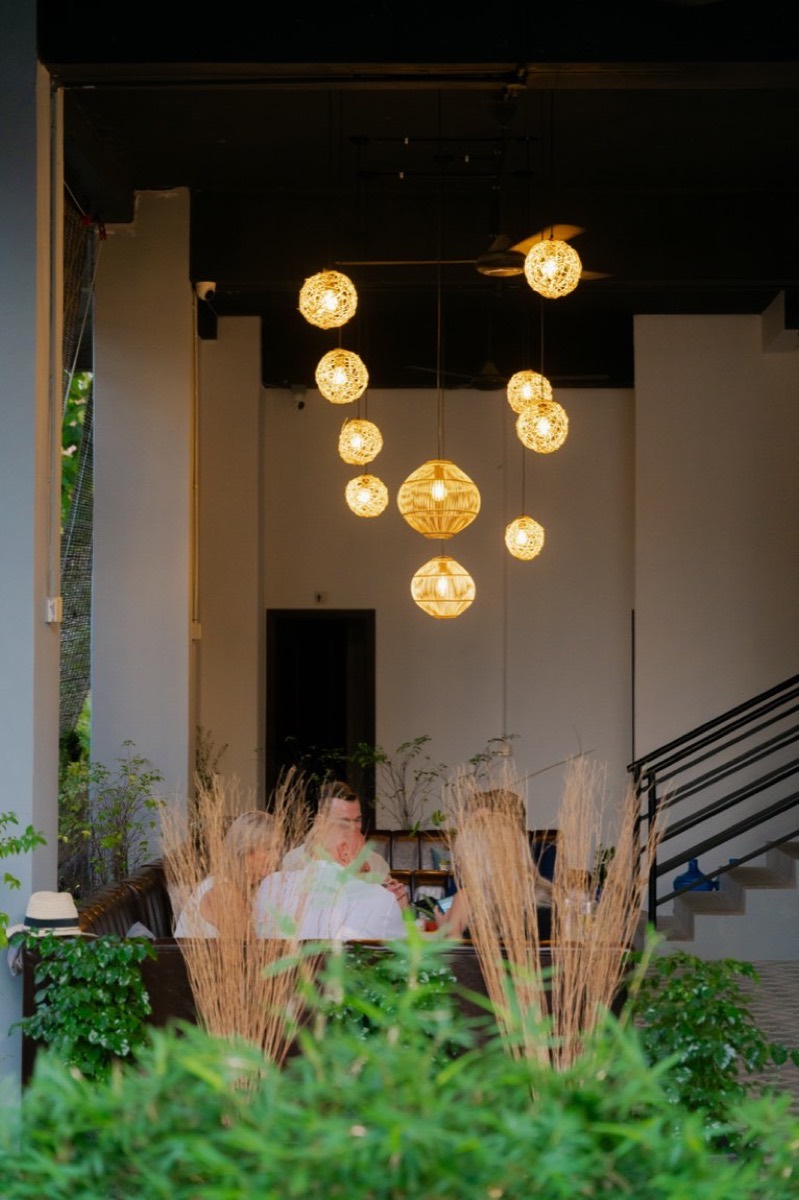 Nomad at dusk, clustered rattan lanterns over booth seating framed by plants
